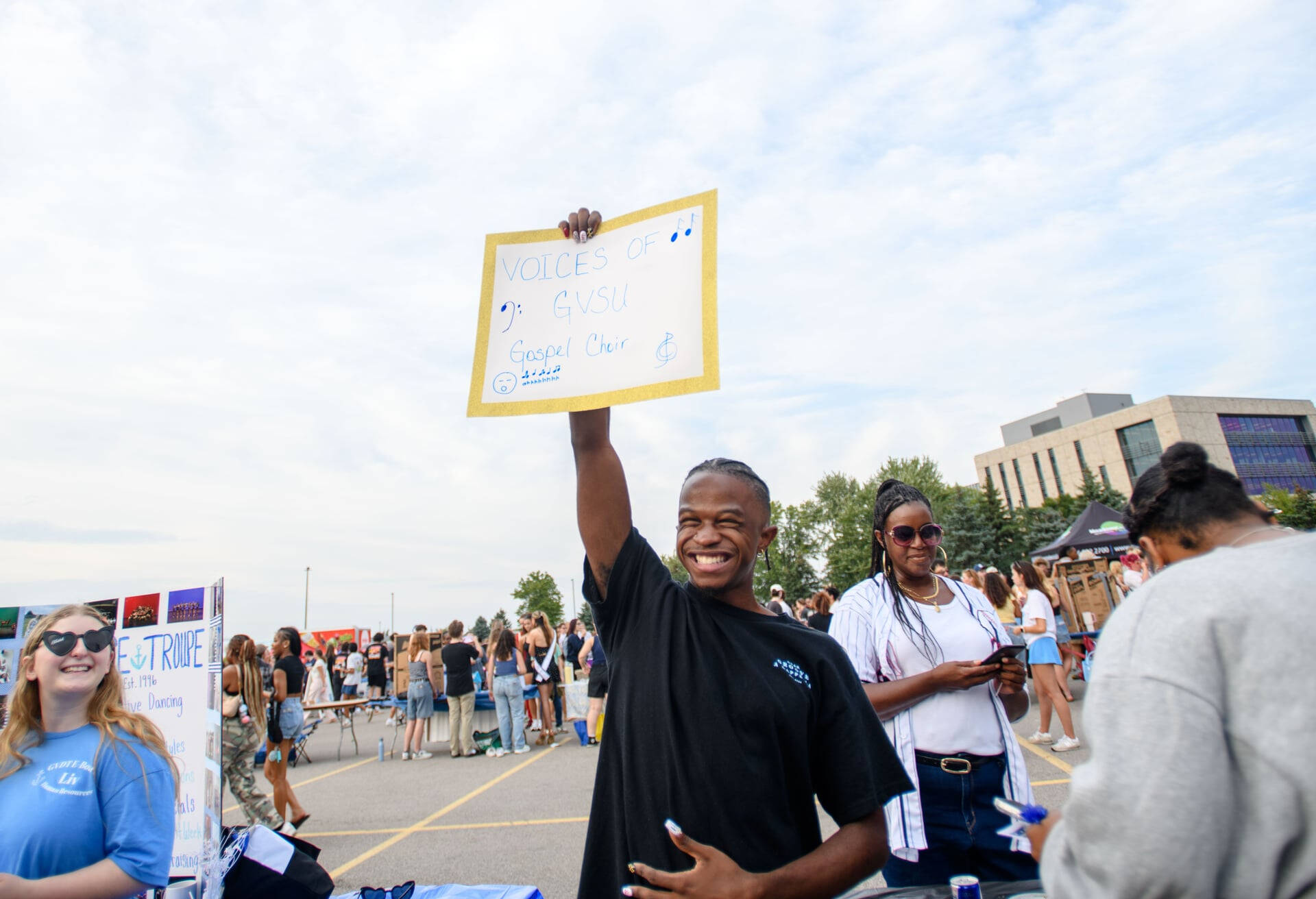 student holds sign for GVSU gospel choir table at Campus Life Night